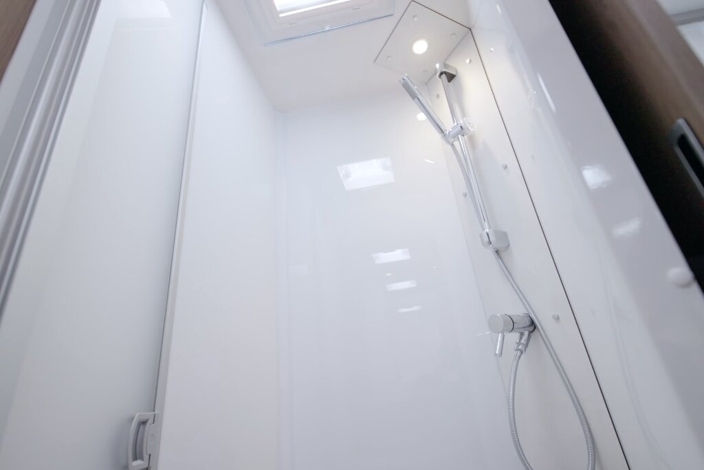 Shower cubicle in the Carado motorhome with hand shower, white walls and roof vent