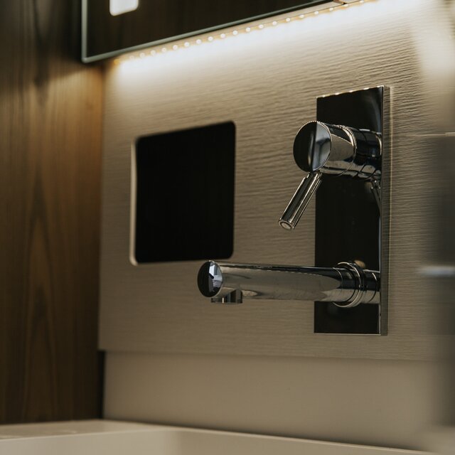 Sink area with wall-mounted faucet and LED lighting on the mirror cabinet above in a motorhome