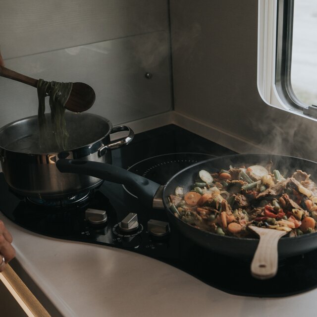 Preparing food (pasta in a saucepan and vegetables in a pan) on a hybrid stove in an RV