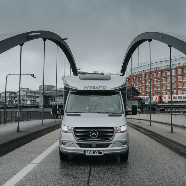 Front view of a semi-integrated HYMER motorhome on an urban bridge in cloudy weather