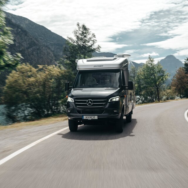 HYMER ML-T syns framifrån när den kör runt en kurva. Miljön är suddig på grund av rörelsen.